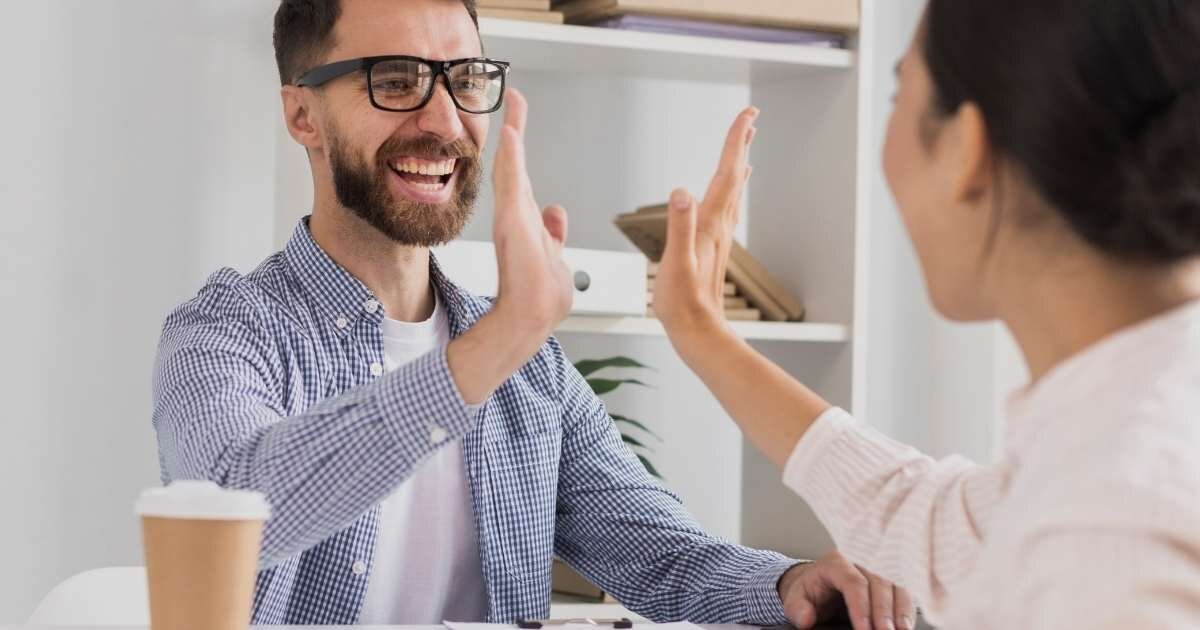 Two smiling coworkers giving a high-five in an office setting, celebrating success